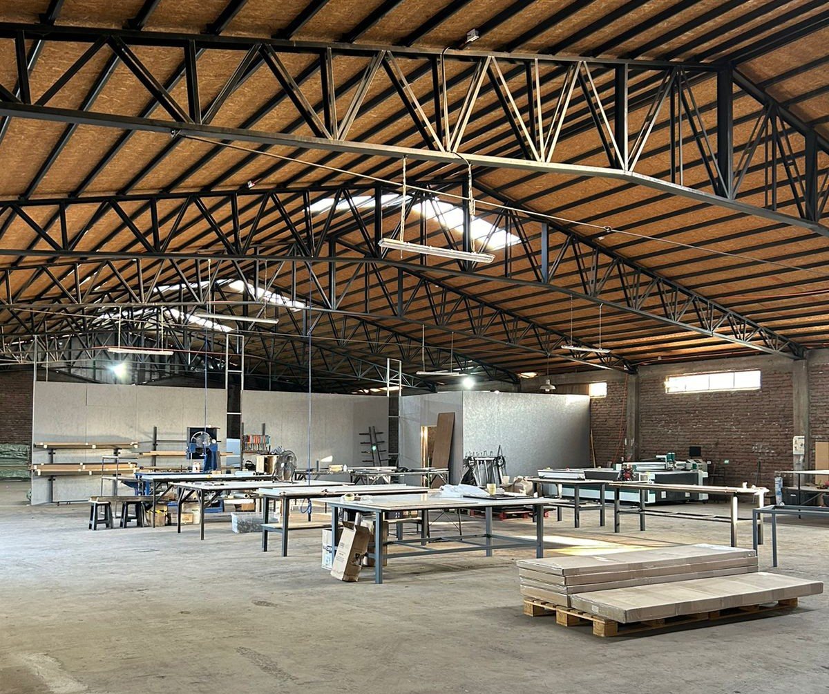 Interior del taller de Wooden Panel en Calera de Tango: mesas de trabajo y CNC bajo cerchas de acero